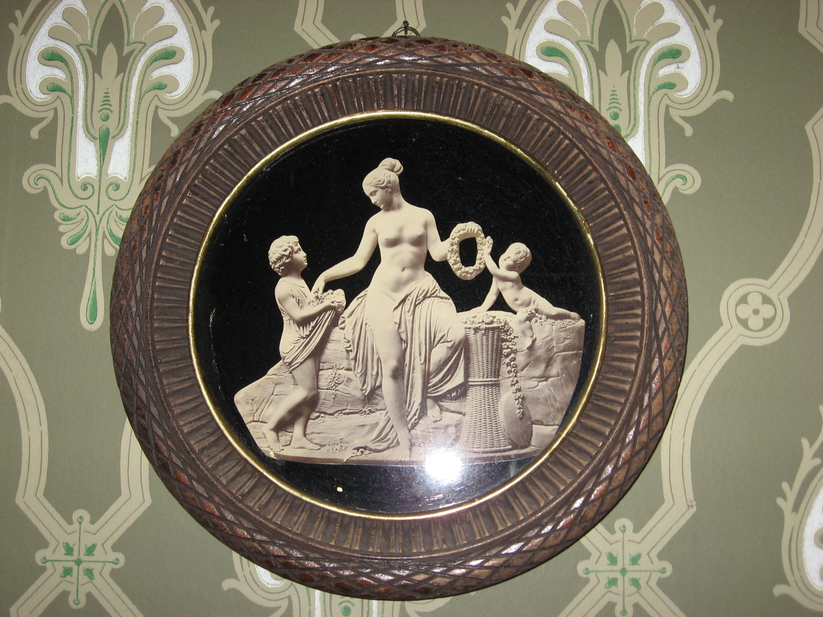 Våren: En kvinne fletter blomsterkrans. To barn, det ene kommer frem med fanget fullt av blomster.