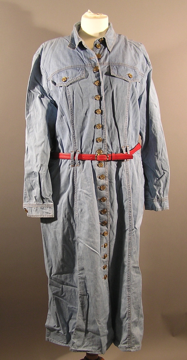 Lang kjole med lang erme, krave, og legg som minner om en arbeidsskjorte. Innsvinget i livet med stropper til belte. Skulder puter. Belte med. Stikklommer i sidenene og 2 klaffer som dekor på forstykket. Knappelukking foran. Splitt i siden på skjørtet.