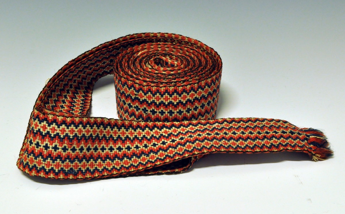 Fra protokollen:
Vævet bælte i hvitt, blaat og rødt. Belte til kvinnedrakt vove i krokbragd, "krokbelte". Tidleg 1800-talet.

Belte i rødt, hvitt og blått - vevet i krokbragdteknikk.