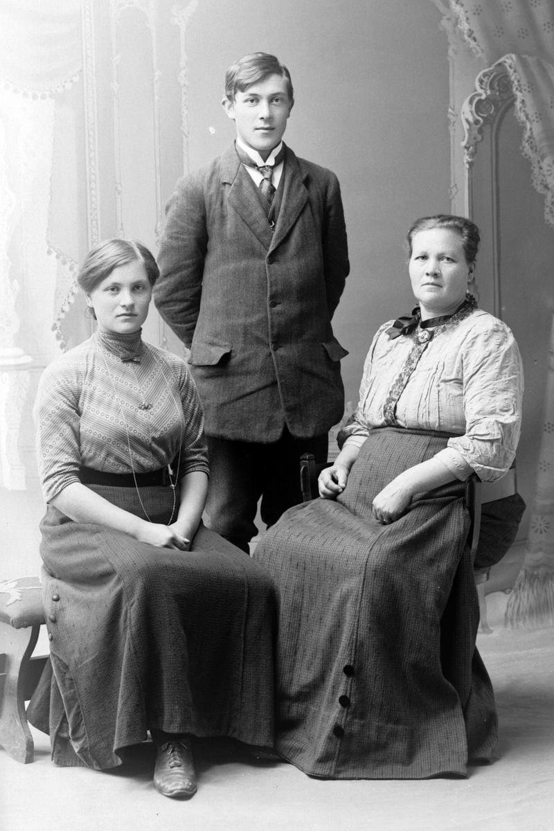 Studioportrett av to sittende kvinner med en stående mann.