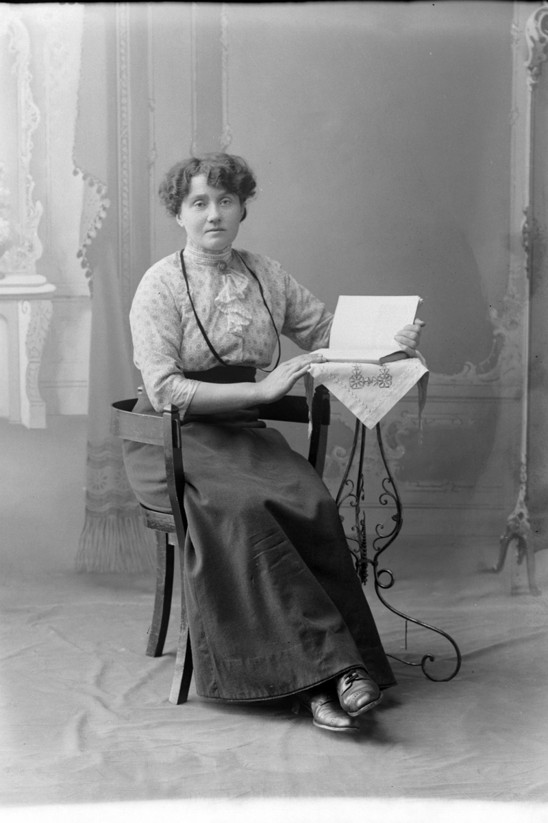 Studioportrett av en kvinne med en bok foran seg.