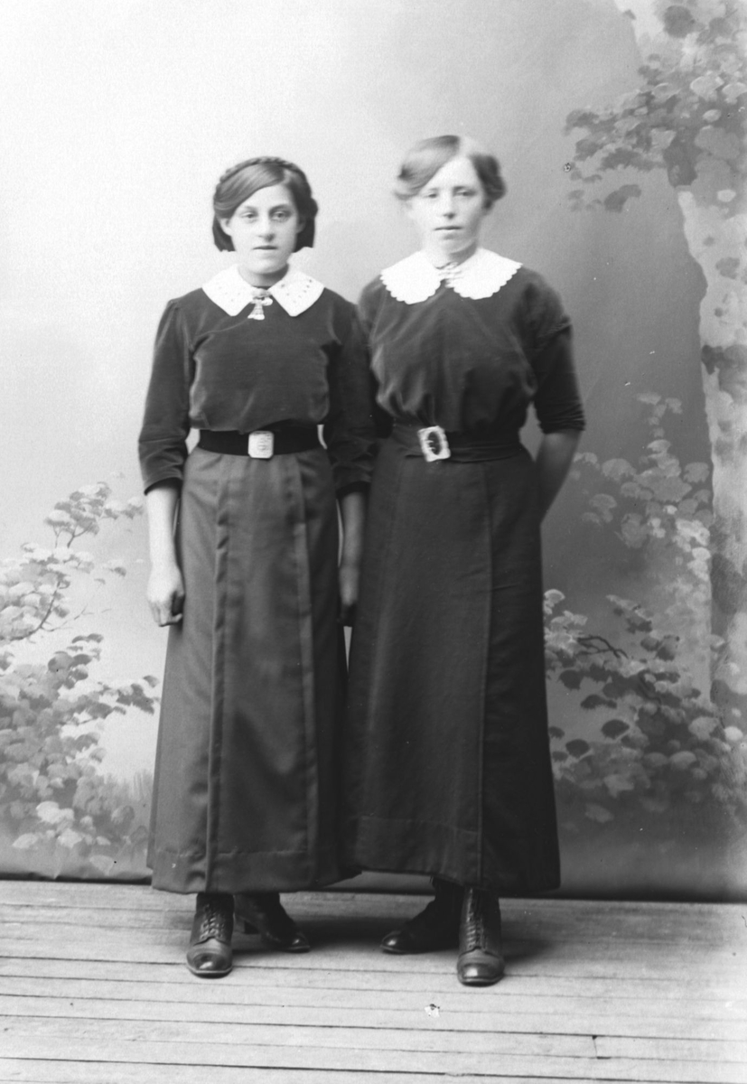 Studioportrett av to kvinner i like kjoler.