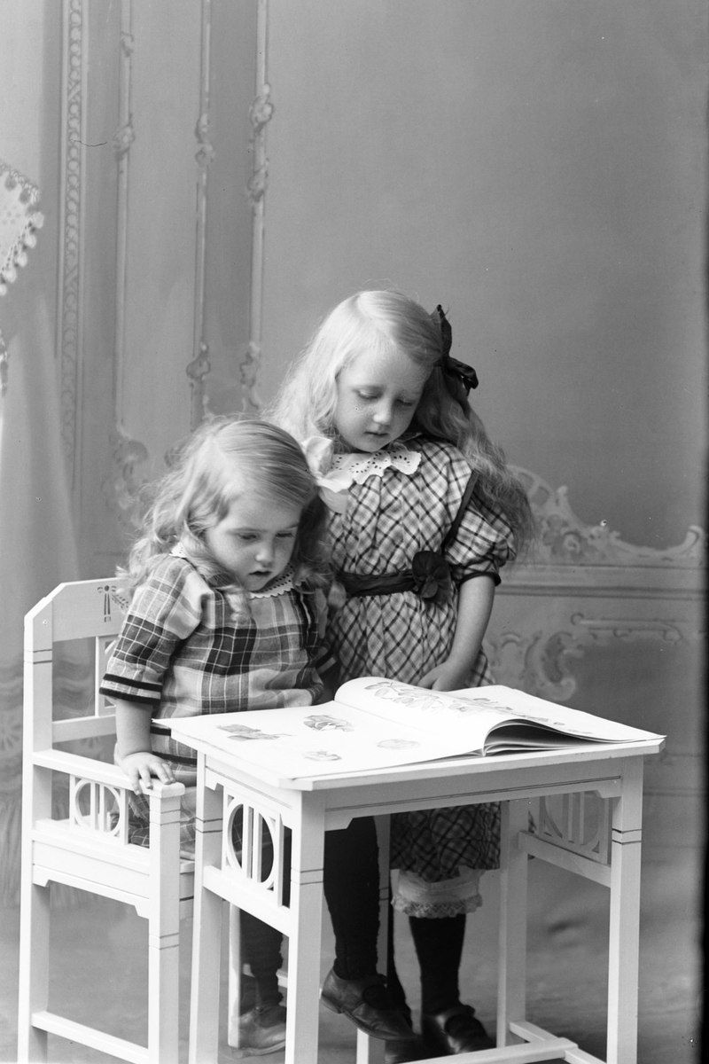 Studioportrett av to jenter som leser en bok.