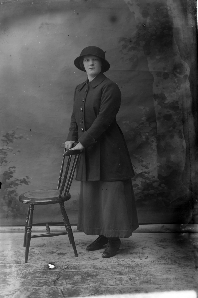 Studioportrett av en kvinne med begge hendene på en stolrygg.