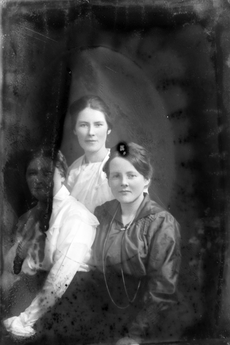 Studioportrett av tre kvinner. Bildet er delvis ødelagt.