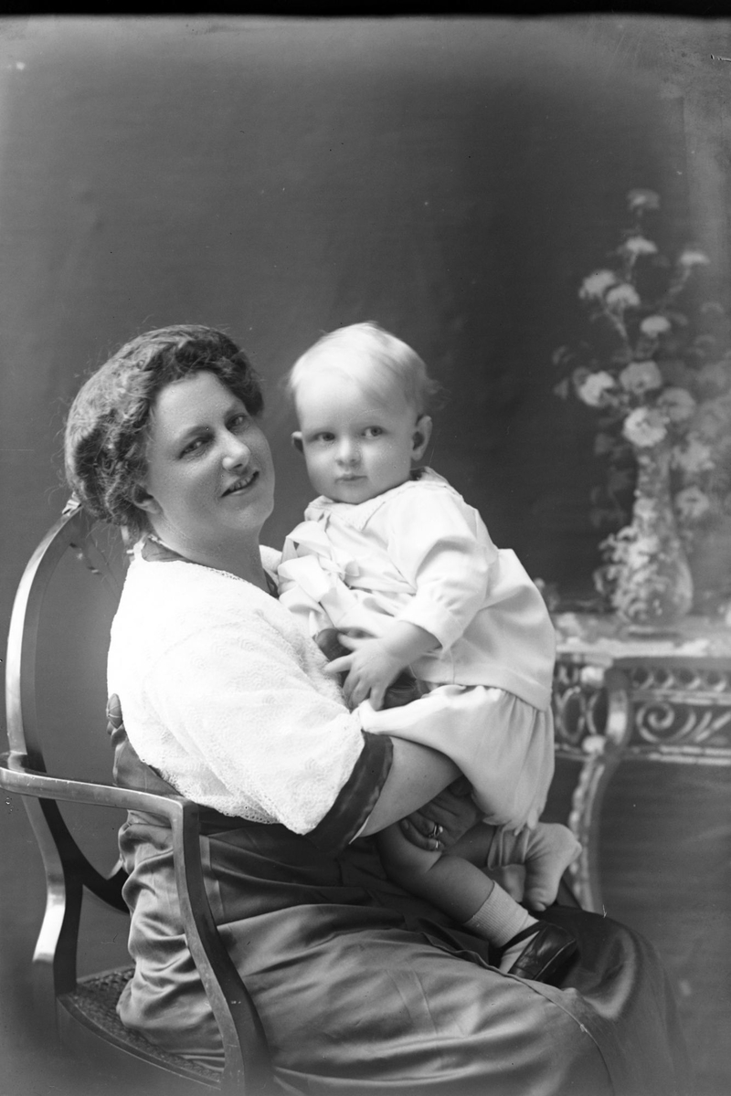 Studioportrett av en sittende kvinne med et barn i armene.