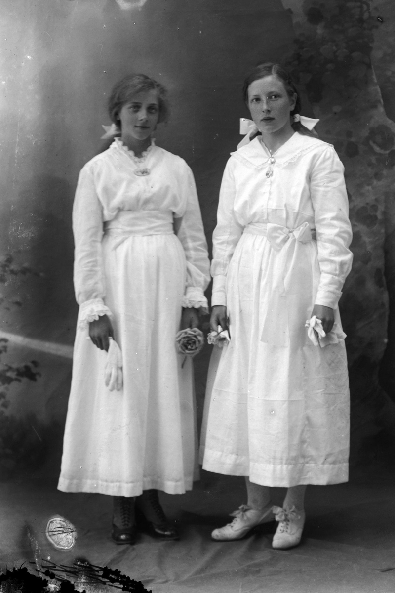 Studioportrett av to kvinner i hvite kjoler.