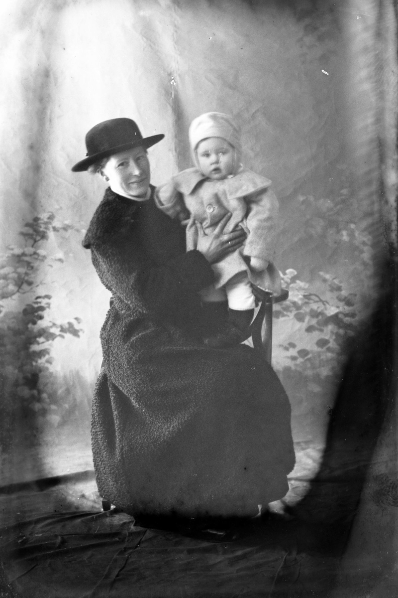 Studioportrett av en kvinne med et barn i armene.