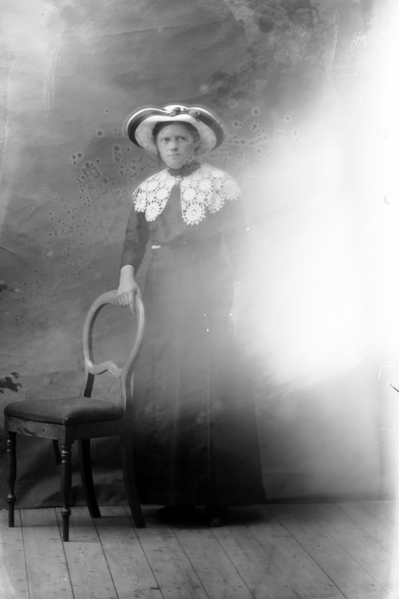 Studioportrett av en kvinne med hatt og en heklet krage. Bildet er delvis ødelagt.