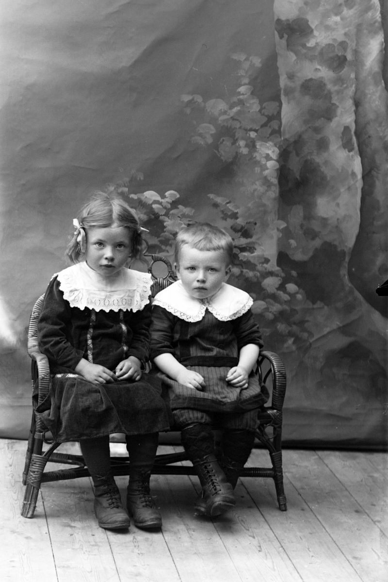 Studioportrett av to barn sittende på en benk.