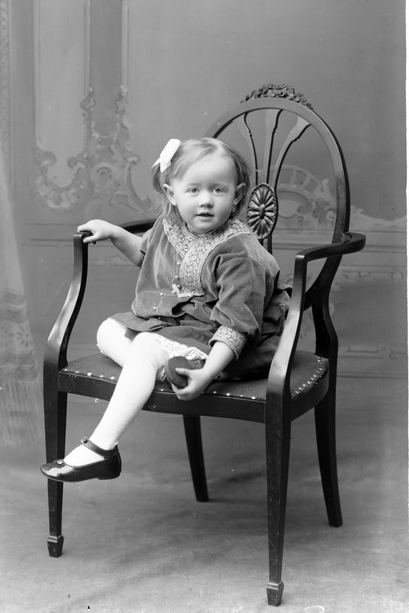 Studioportrett av en ung jente sittende på en stol.