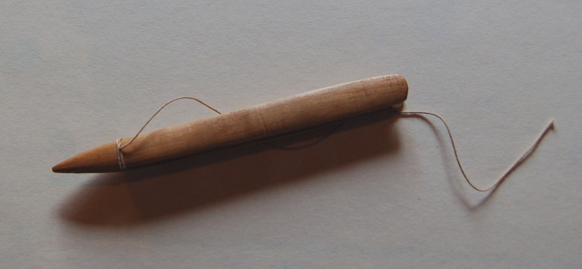 Nålen har en rektangulær form. I nålen er det utfreset et spor som tråden skal spoles opp på, og munnen på nålen er nebbformet med splittet ende.                                                                          På nålen er det en rest av bøtingstråd.