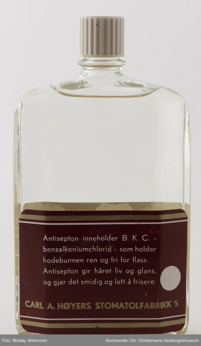 Glassflaske med skrukork. Innhold:  Antisepton hårvann, uten fett.