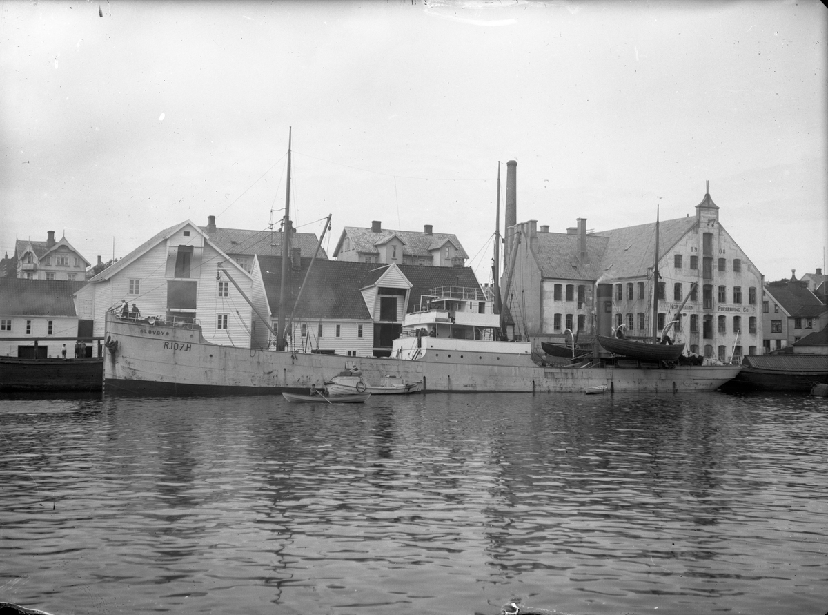 Damskipet D/S "Løvøy" ved kai i det som antageligvis er Bergen. Bak til høyre ligger industribygget til "Norwegian Preserving Co.".