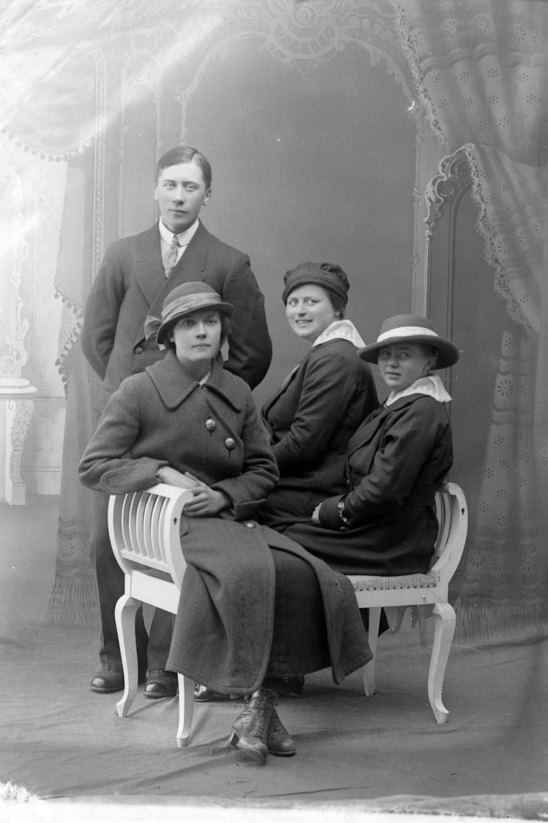 Studioportrett av tre kvinner som sitter foran en stående mann.