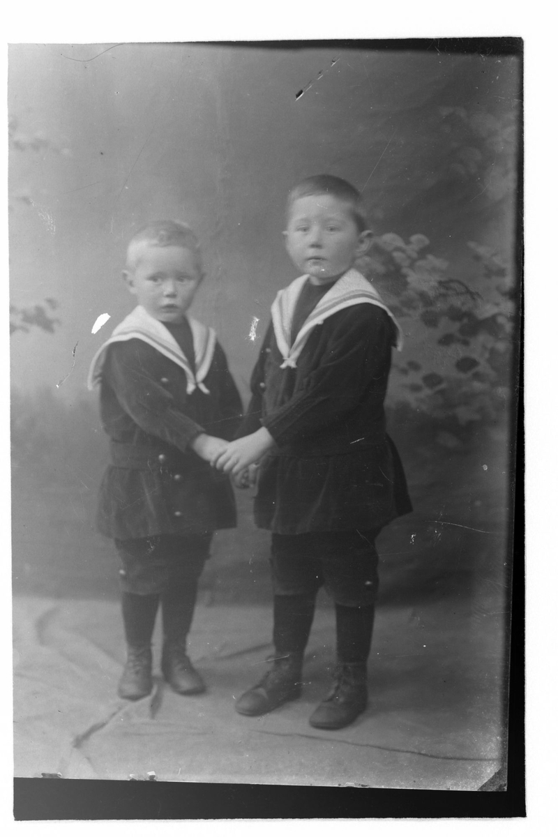 Studioportrett av to gutter kledd i matrosdresser.