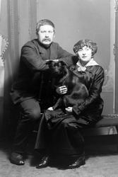 Studioportrett av to personer med en hund.