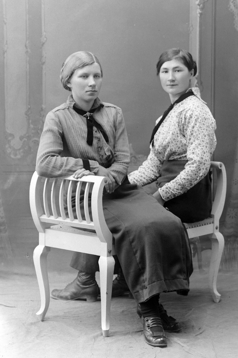 Studioportrett av to kvinner som sitter på en benk.