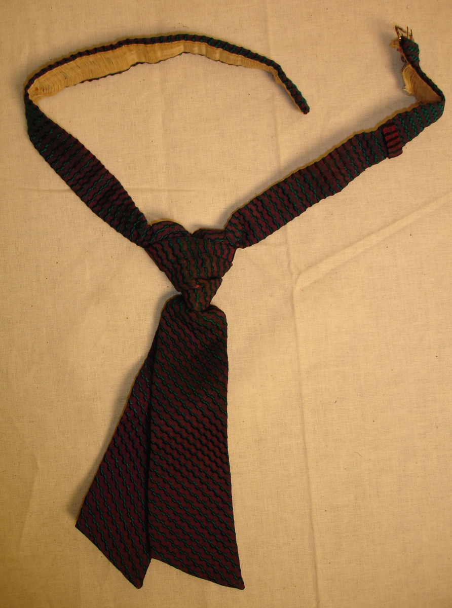 Slips, ferdigknyttet, med metallspenne til å feste bak under skjortekragen. Lengde 20 cm fra og med knuten.