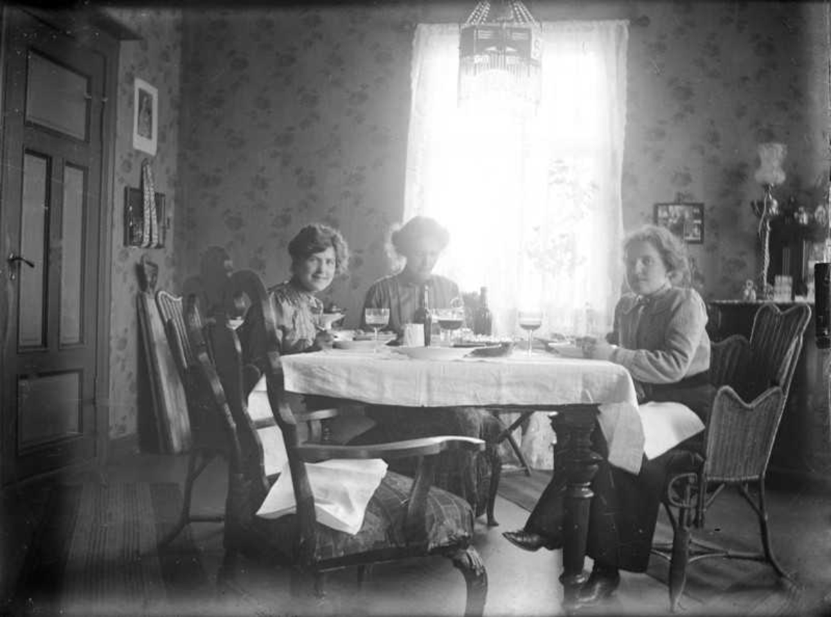 Tre damer sitter inne ved et  bord. Claudia til venstre og Anna til høyre.
