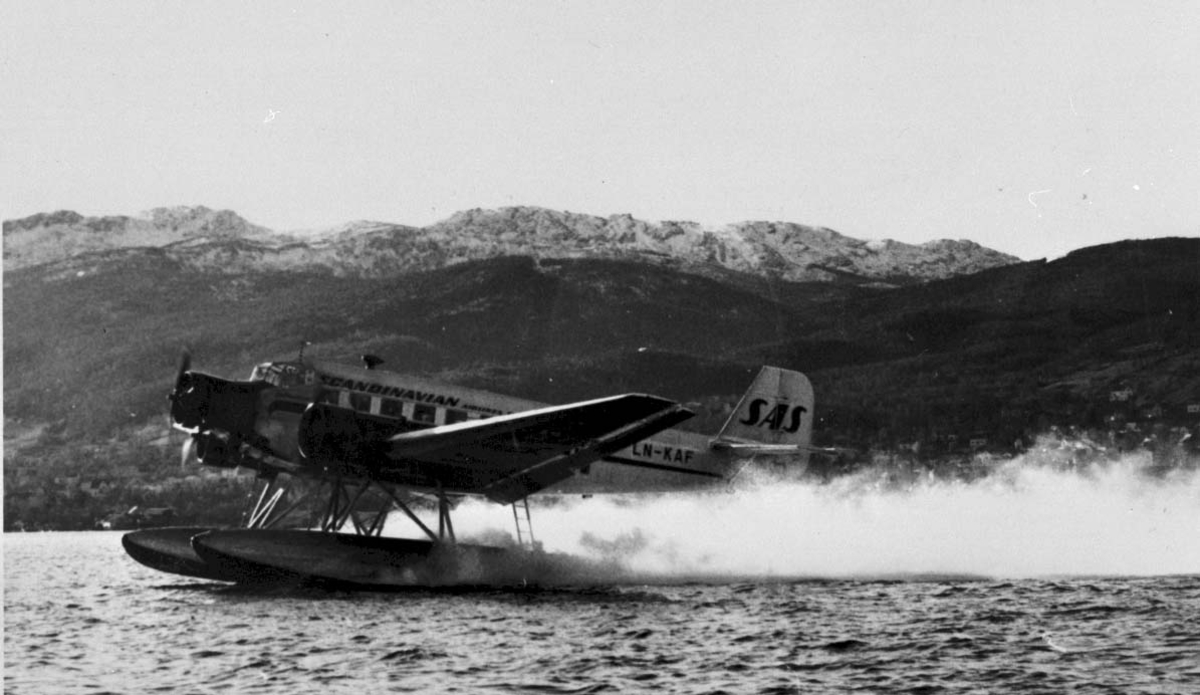 1 fly i fart på havet, Junkers Ju52 3m mg LN-KAF "Askeladden" fra DNL (merket SAS). Bebyggelse i bakgrunnen.