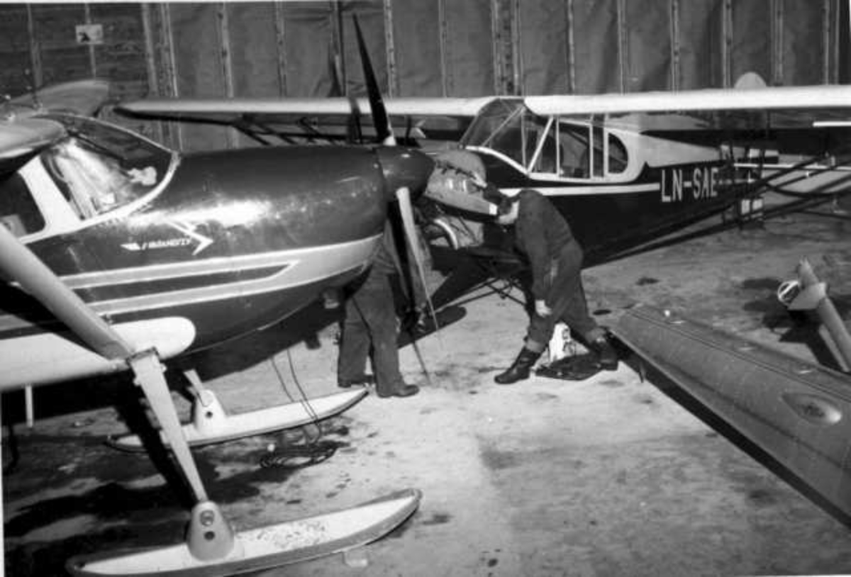To fly og noe utstyr inne i en hangar. En person ved flyene. Flyet bak er LN-SAE