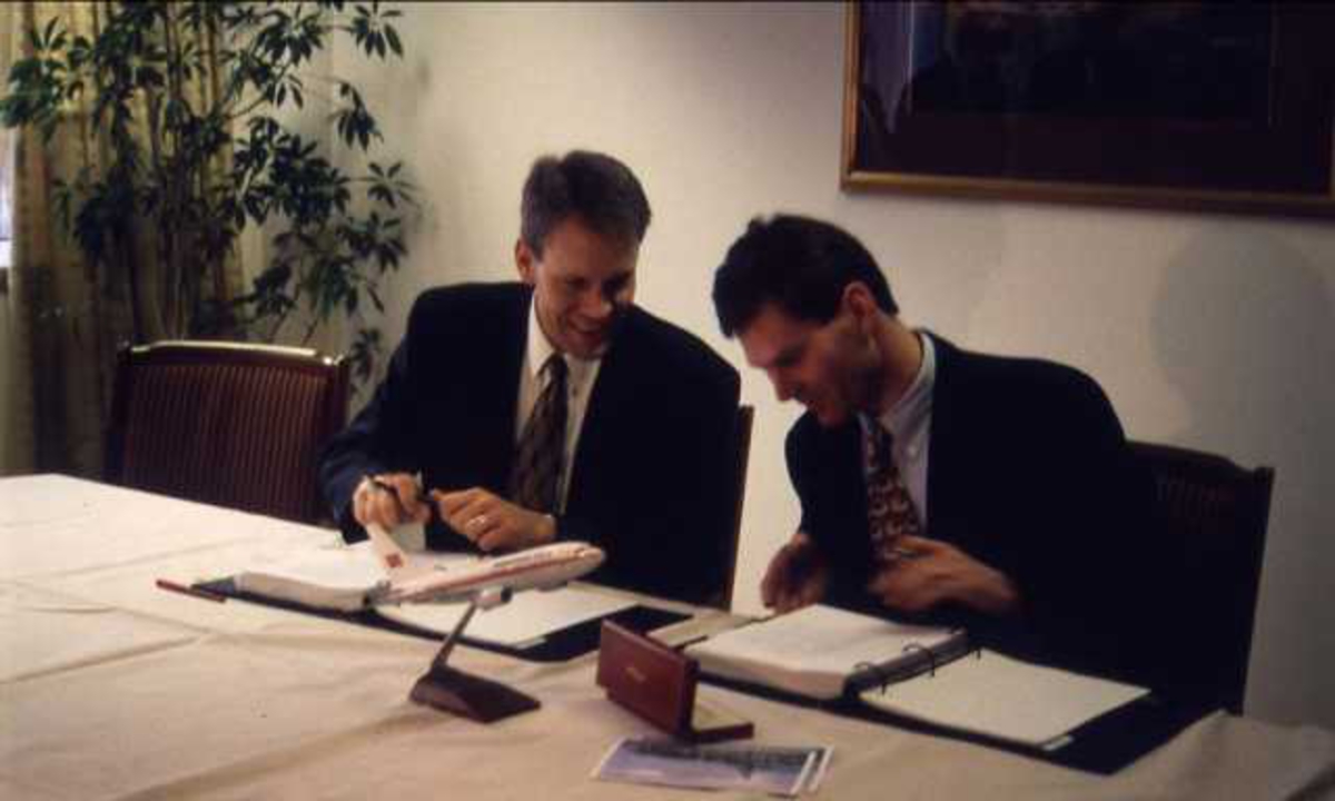 To personer sittende bak bord. Per G. Braathen til høyre. Signering av paprirer.
