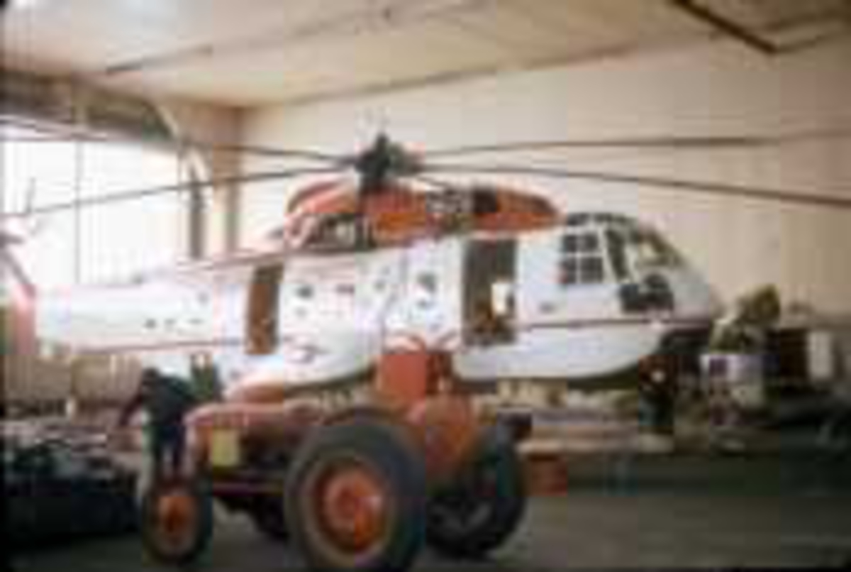1 helikopter inne i en hangar. Sikorsky S-61N MkII, LN-OSK fra Helikopter Service. 1 traktor og 1 person foran helikoptret.
