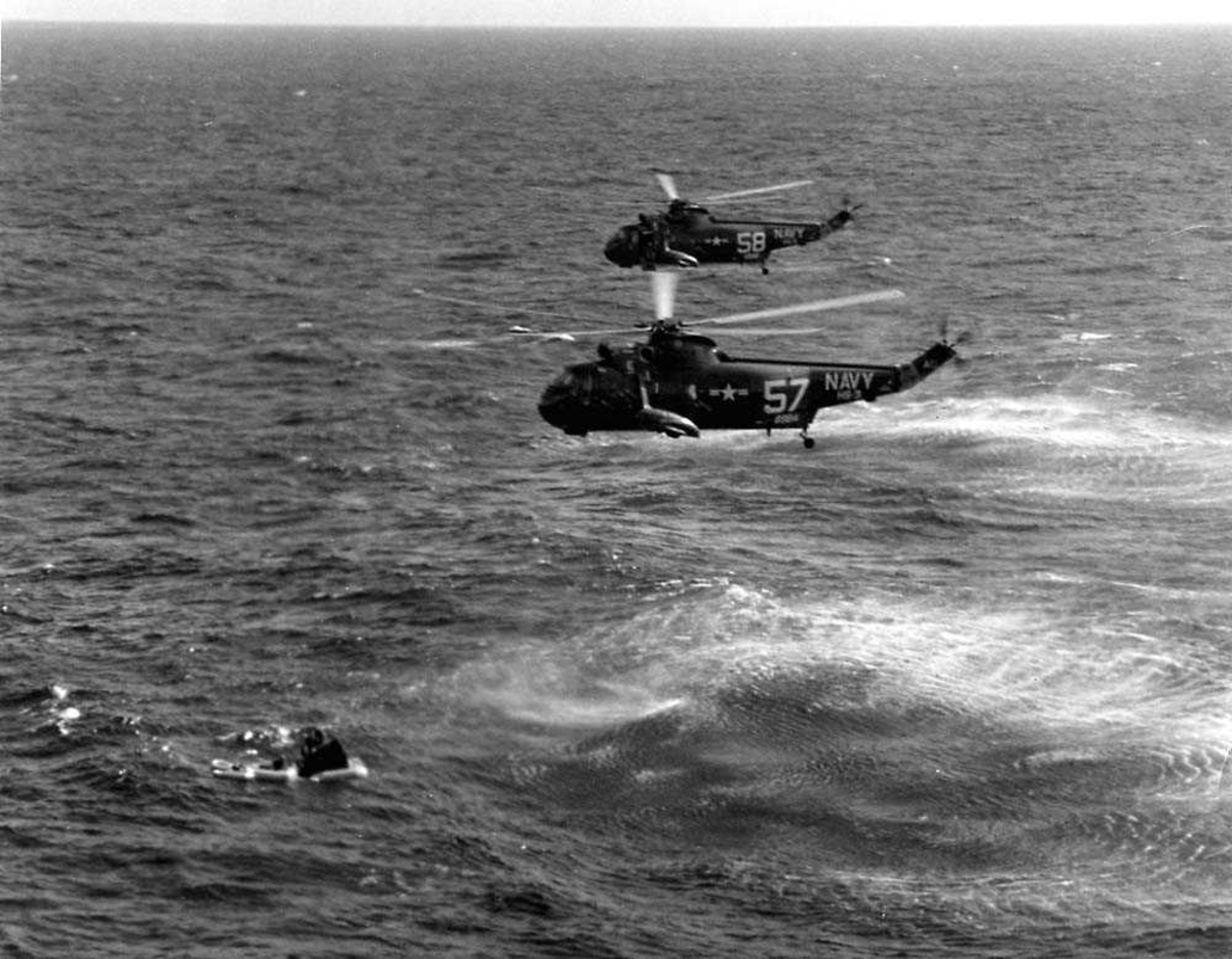 Luftfoto. To helikoptere i luften, Sirkorsky Sea King SH-3A fra US Navy. Ett romfartøy, Gemini 3, ligger i sjøen under helikoptrerne.