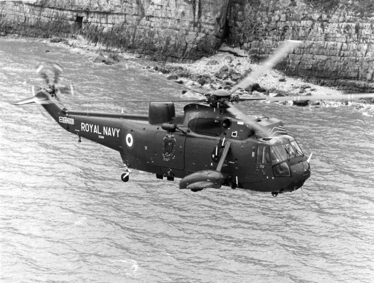 Ett helikopter i luften, ved kysten. Westland Sea King Mk.5, tilhørende Royal Navy merket XZ916.