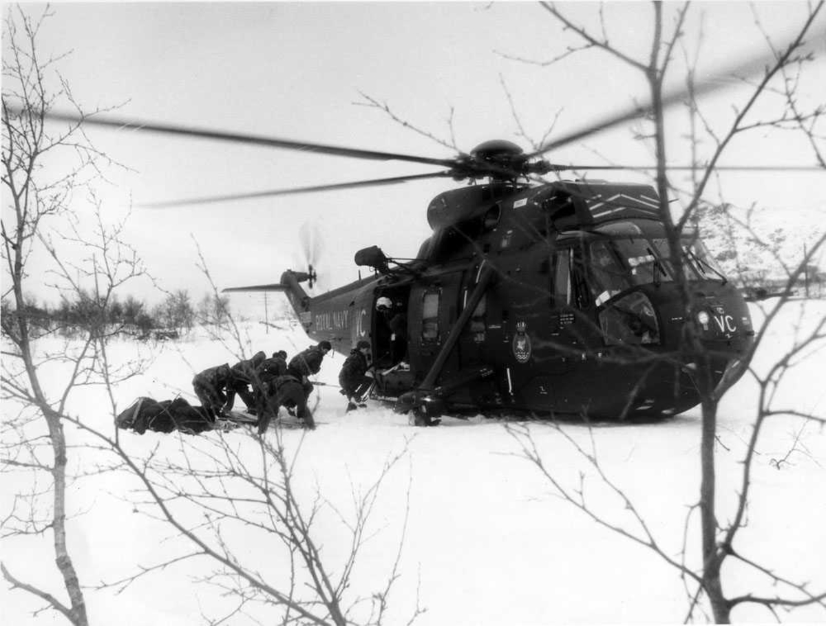 Ett helikopter på bakken, snødekke, soldater på vei inn i helikopteret. Westland Sea King Mk.4 tilhørende Royal Navy.