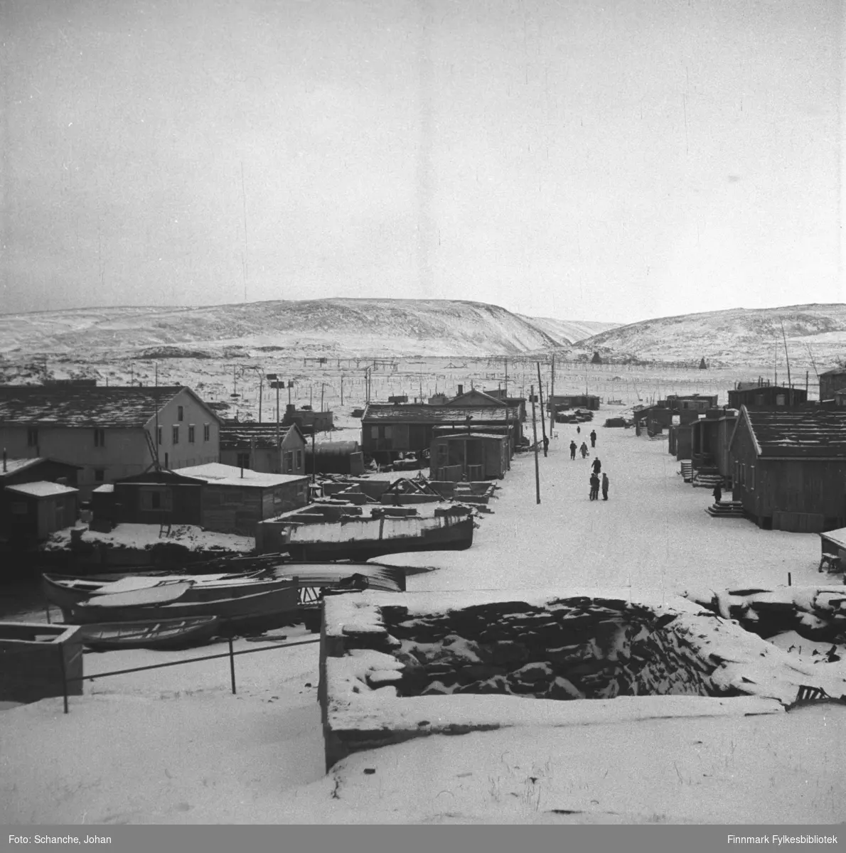 Oversiktsbilde fra Berlevåg i gjenreisningstid. Foran på bildet ruiner,  gate, noen mennesker på gata.  På begge sider av gaten står det byggninger, ruiner og boliger under bygging.