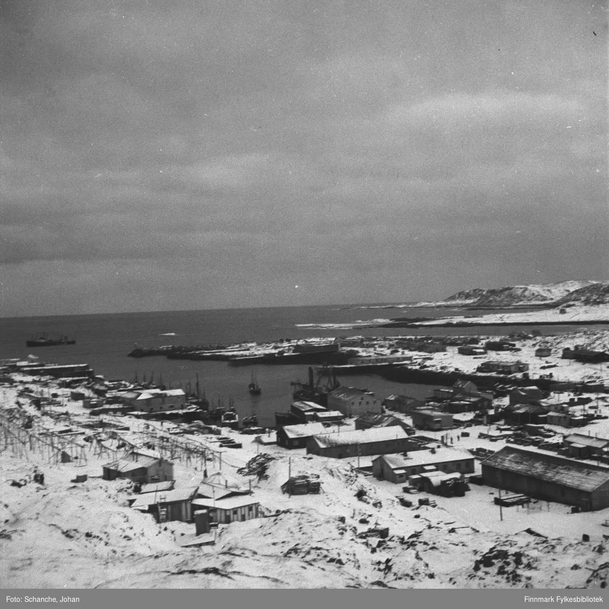 Oversiktsbilde fra Berlevåg i gjenreisningstid.  På bildet ses nesten hele byen slik den var 1948. Bildet er tatt fra fjellet. Noen båter ligger på kai, et skip ut i havet.
