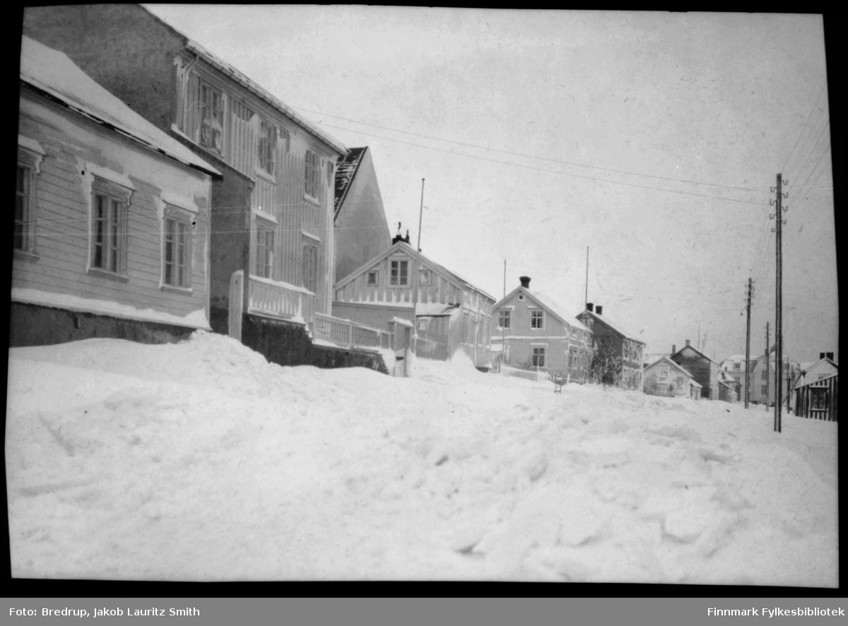 Inspektør Hansens gate i Vadsø.  Det har vært snøstorm, og husene er dekket med snø.  Midt i bildet en forlatt spark, den står forlatt omtrent der Kirkebakken krysser Inspektør Hansensgate