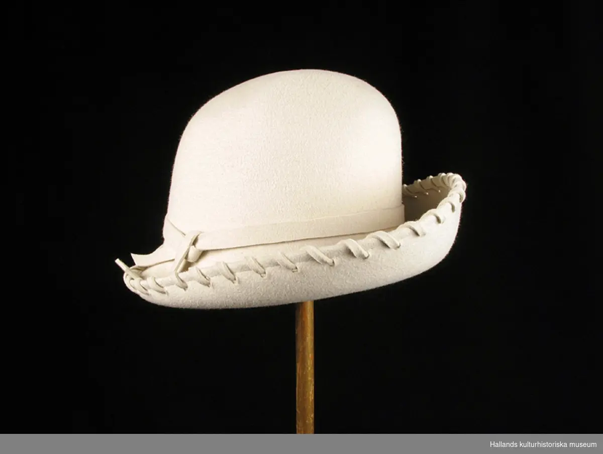 Cremefärgad, rund damhatt i filt. Hatten är lite vidare på höger sida och där knyts också ett filtband som löper runt hatten. Utmed ytterkanten är det sytt med ett filtband (cowboyhatt-känsla).