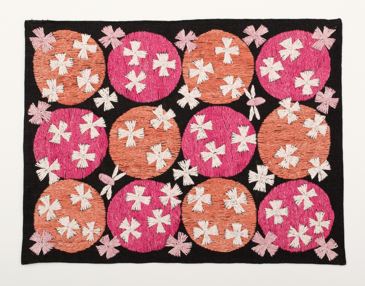 Rektangulär duk på svart linnebotten, fodrad med blekt linnetyg. Motiv med tre x fyra cirklar (en cirkel = 67 mm) i två olika rosa lingarner. Två flygfän fladdrar omkring. Fyrbladiga blommor över både rosa cirklar och svart botten.