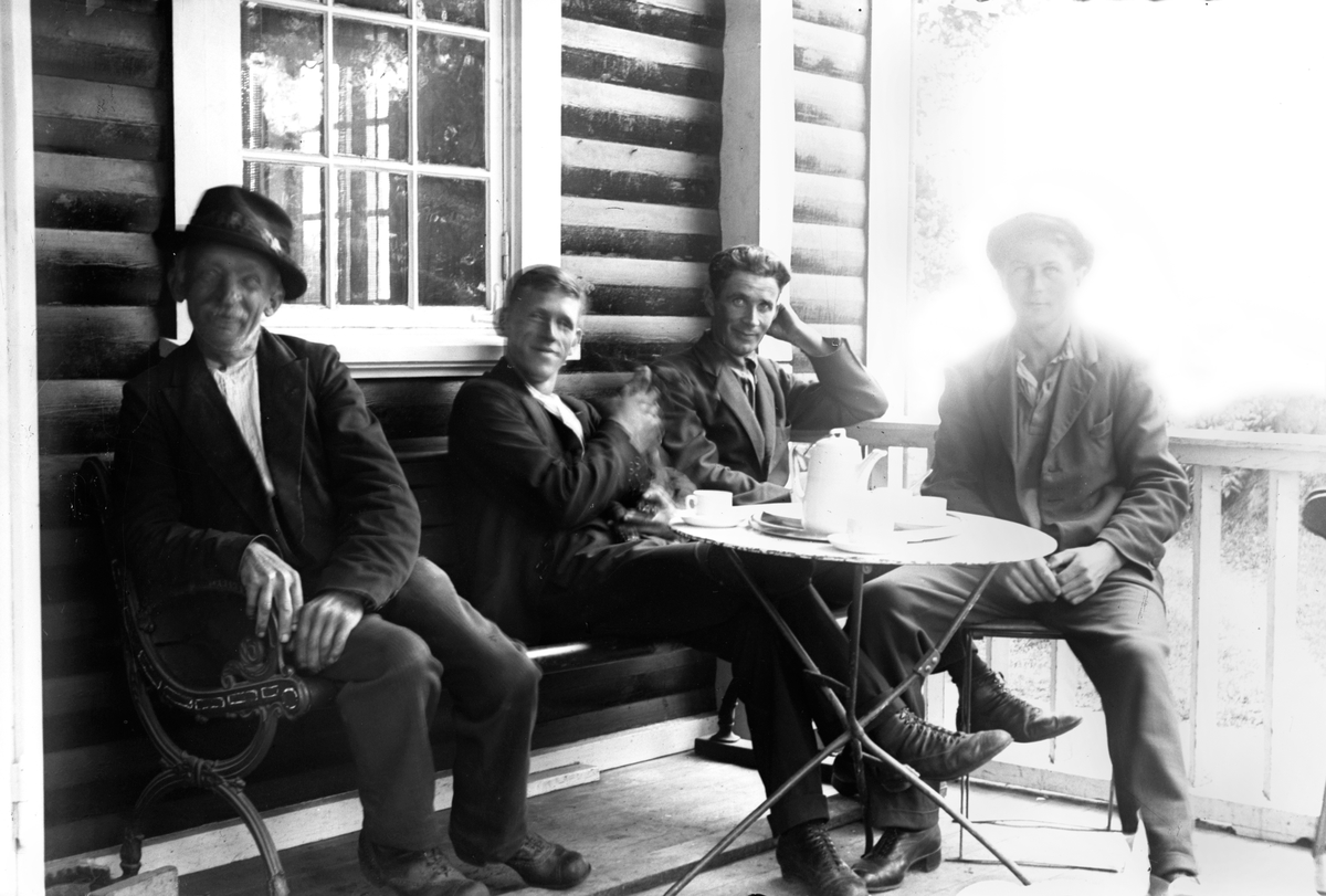 Fyra män sitter runt ett bord och dricker kaffe.
