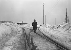 Mann med hatt som spaserer i jernbanesporene på dampskipskai