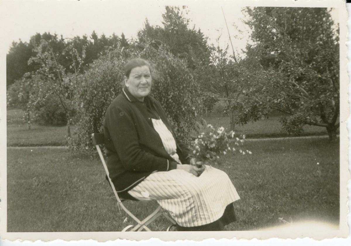 Kristina Eliasson i trädgård med blommor i hand.  Lerdal