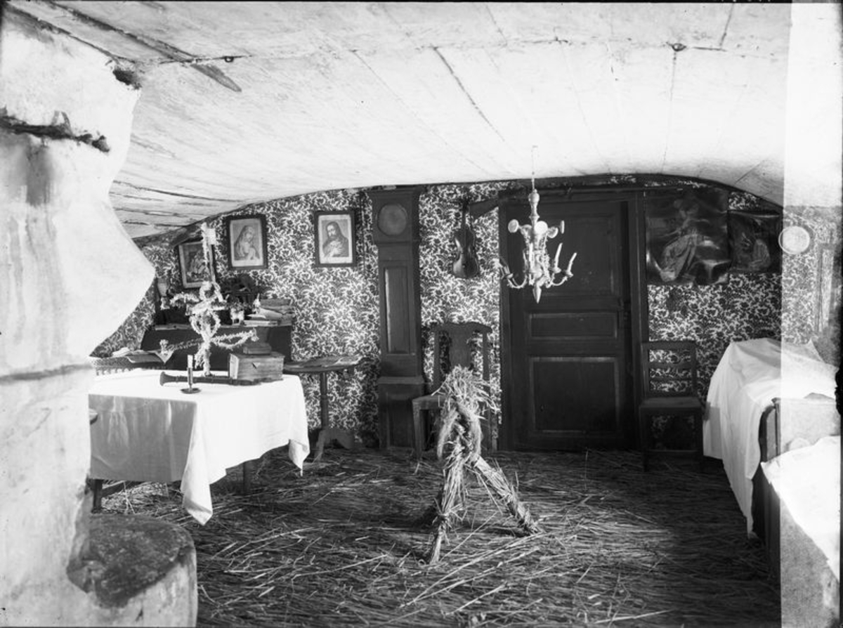 Interiör av gamla stugan med julhalm på golvet. I förgrunden Julbocken. Stugan flyttades på 1920-talet till Bitterna.  Mellomgården  Hudene