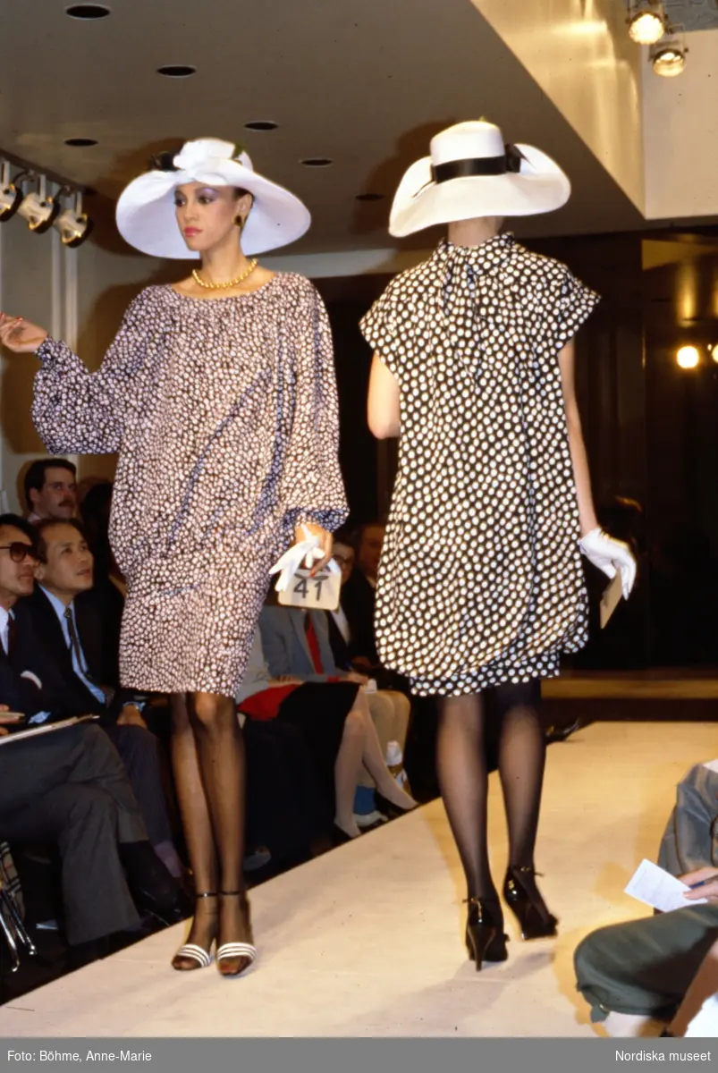 Modevisning. Modeller i prickiga klänningar, vita bredbrättade hattar och vita handskar. Från Givenchy.