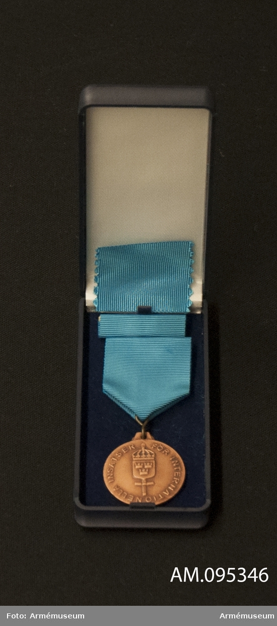 Medalj och släpspänne med blått band i blå ask klädd med mörkblå sammet och vit siden.