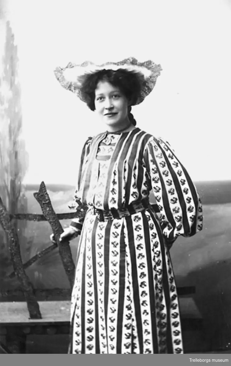 Porträtt av okänd kvinna i mönstrad klänning och hatt.