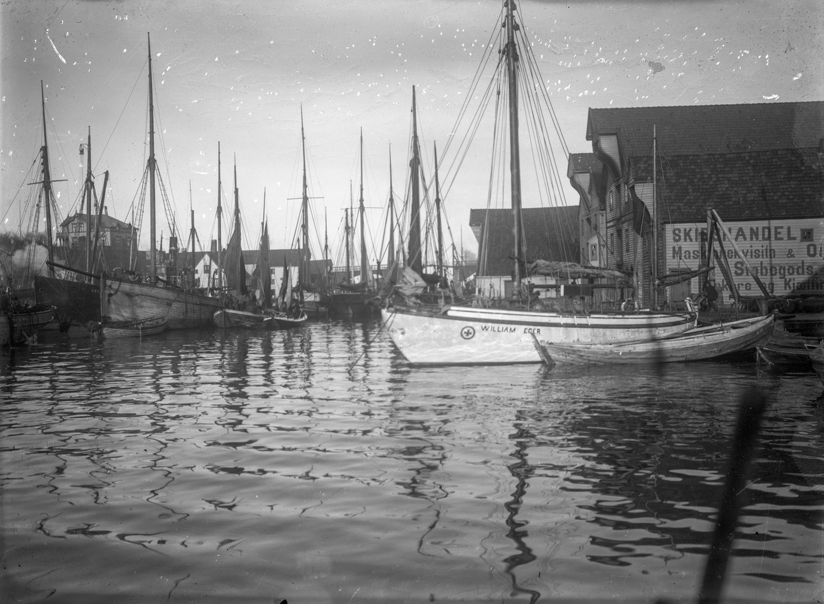 Seilebåter (bl. a." William Egir"), seilskuter og robåter ankret opp ved søndre del Smedasundet i Haugesund. Sjøhus i bakgrunnen. Hasseløybroen i bakgrunnen.