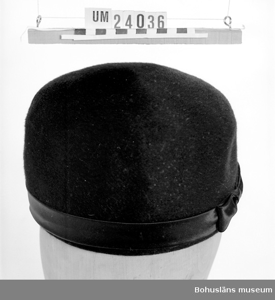 471 Tillverkningstid 1961-1967

Pillerburksmodell. Hög rak hattmodell utan brätten. Svart filt och med svart sidenband längs nederkant. Rosett framtill. Använd vid begravningar. Sorgslöja finns se UM024037.