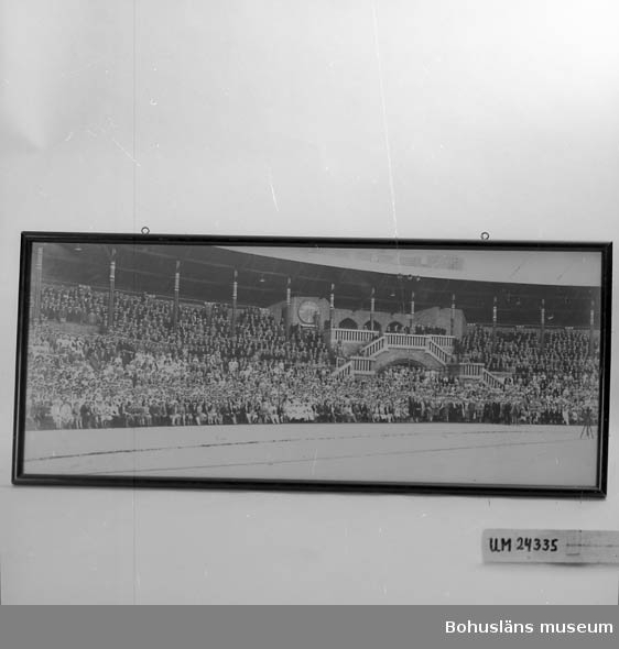 Inramat fotografi (svart/vitt) av 1000 sångare samlade på Stadion, Stockholm. 
Svart ram. I ramens överkant finns två fastskruvade metallöglor