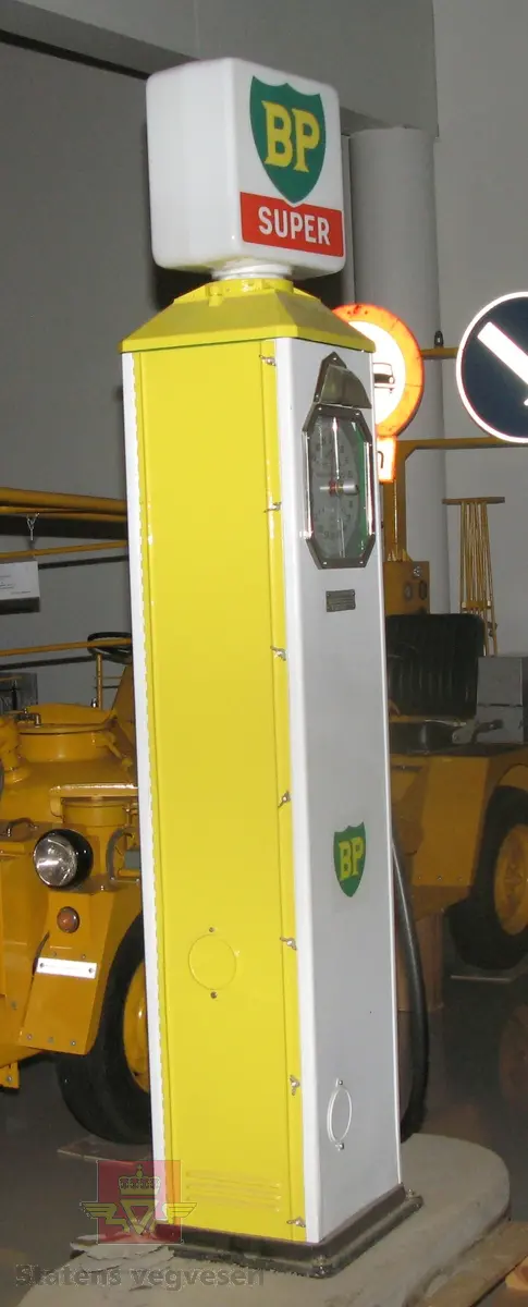 Hovedsakelig hvit og gul bensinpumpe, med logo fra BP. Elektrisk drevet med lyspære i toppen. Kan fylle opptil 100 liter om gangen.  Pumpa har diverse merking. I oppusset stand. Pumpa er montert på en sokkel av betong.