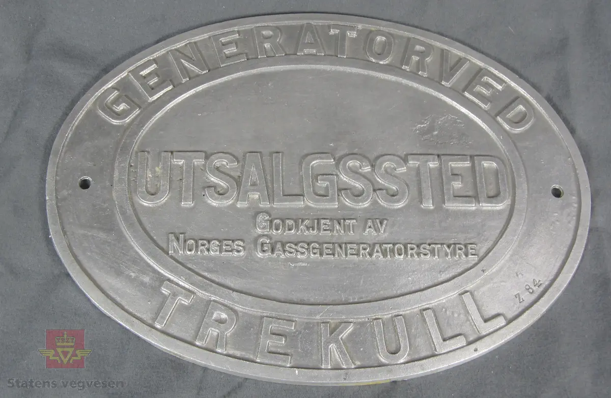 Ovalt skilt av aluminium med to hull for fastsetting. Tekst: GENERATORVED TREKULL UTSALGSSTED GODKJENT AV NORGES GASSGENERATORSTYRE
Z 84.