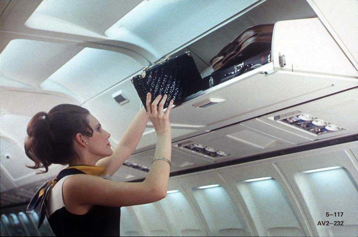 En person som legger en veske oppi hattehyllen på en Boeing 737-200.