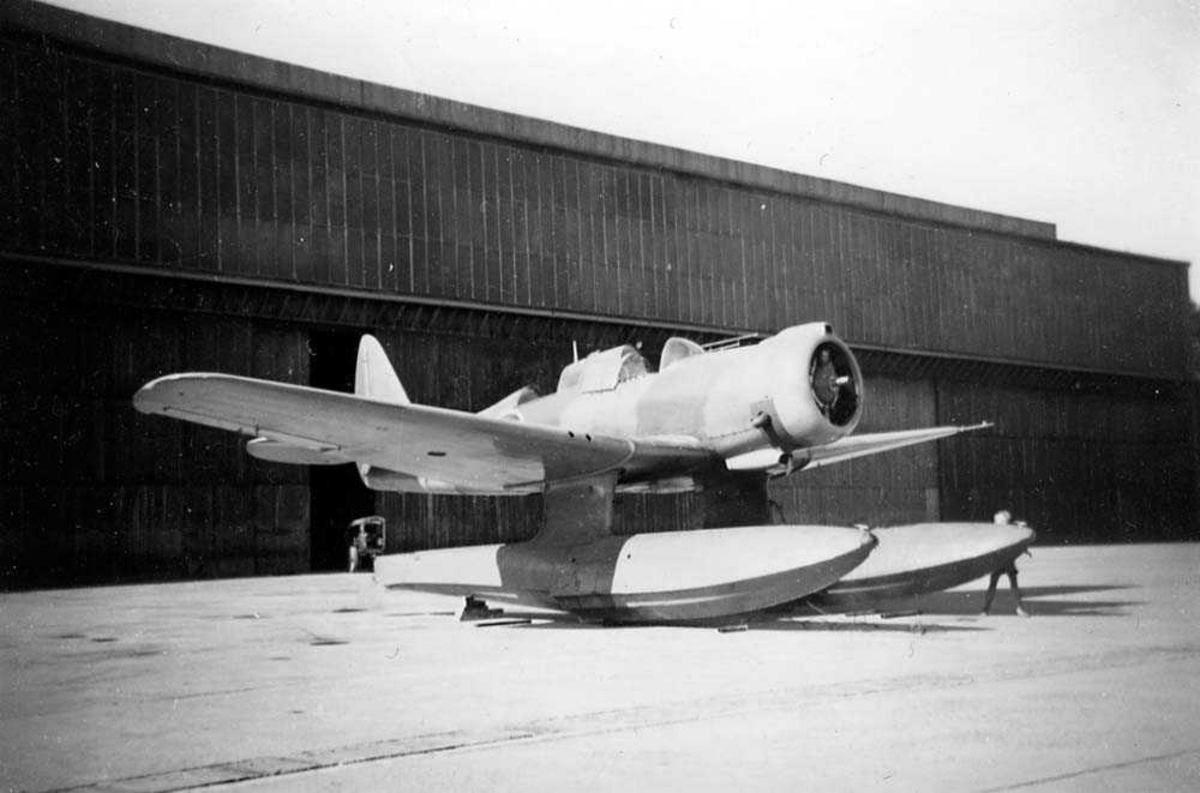 Lufthavn. Ett fly på bakken, Northrop N-3PB med flotører, foran en hangar.